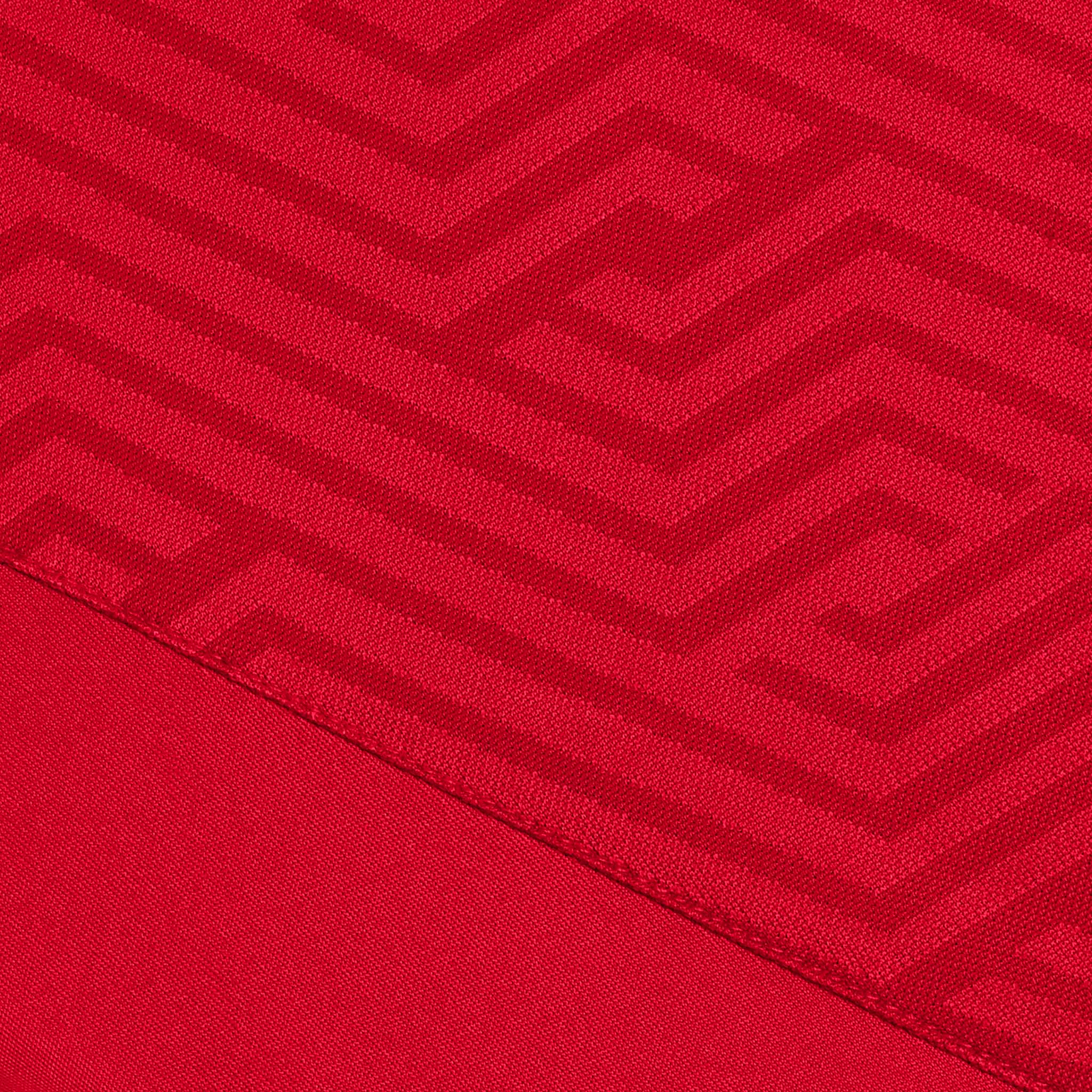 Närbild av röd Player shirt S/S Monaco v24, Match & Training wear, med geometrisk zigzag-textur.