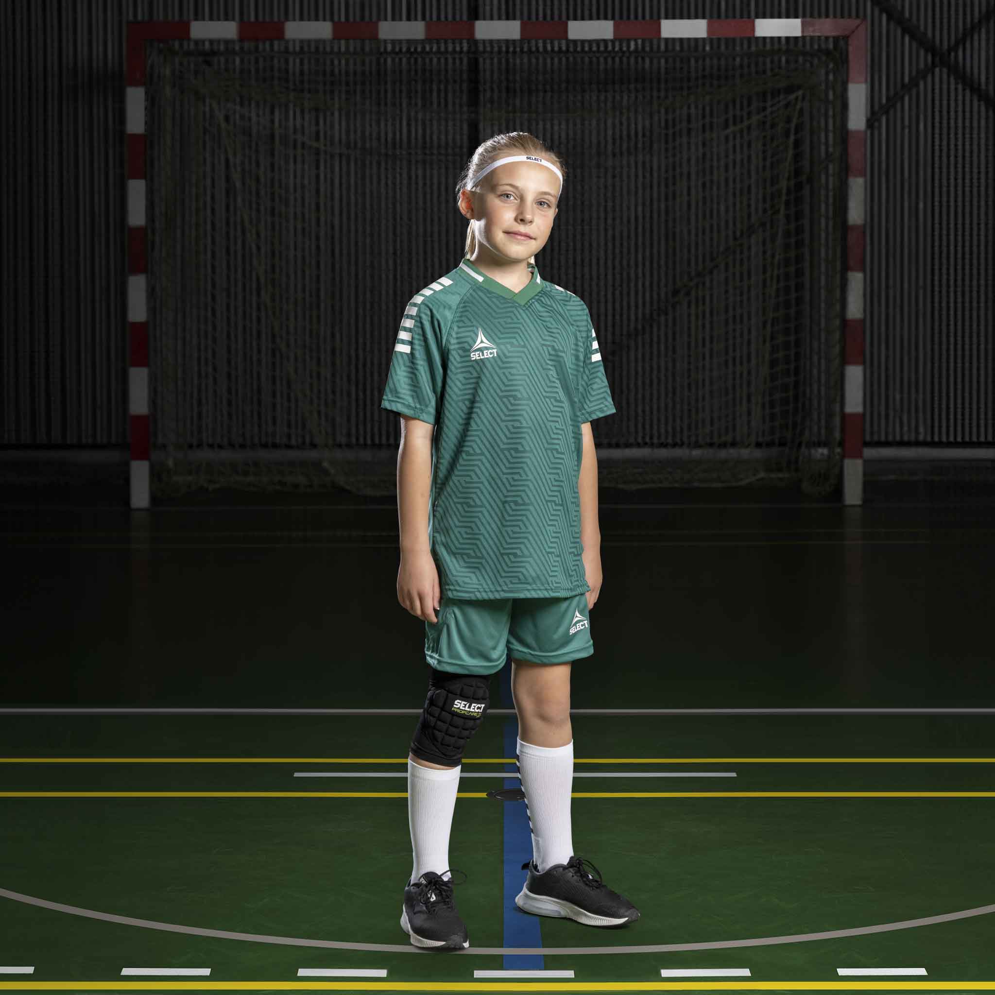 Pojke fotbollsspelare i grön-vita Player shorts Monaco v24, Match & Training wear, framifrån på inomhusplan.