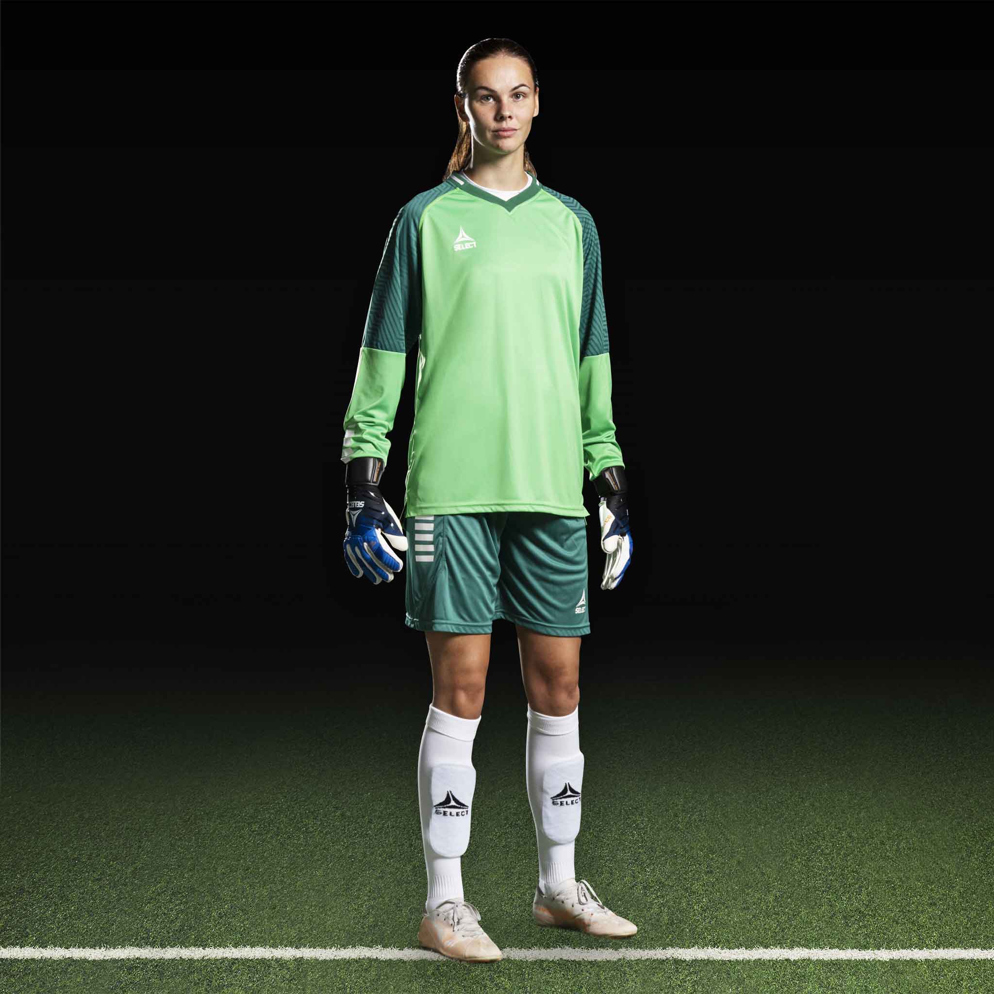 Kvinnlig fotbollsspelare i grön Goalkeeper shirt Monaco v24, målvaktskläder med handskar på plan.