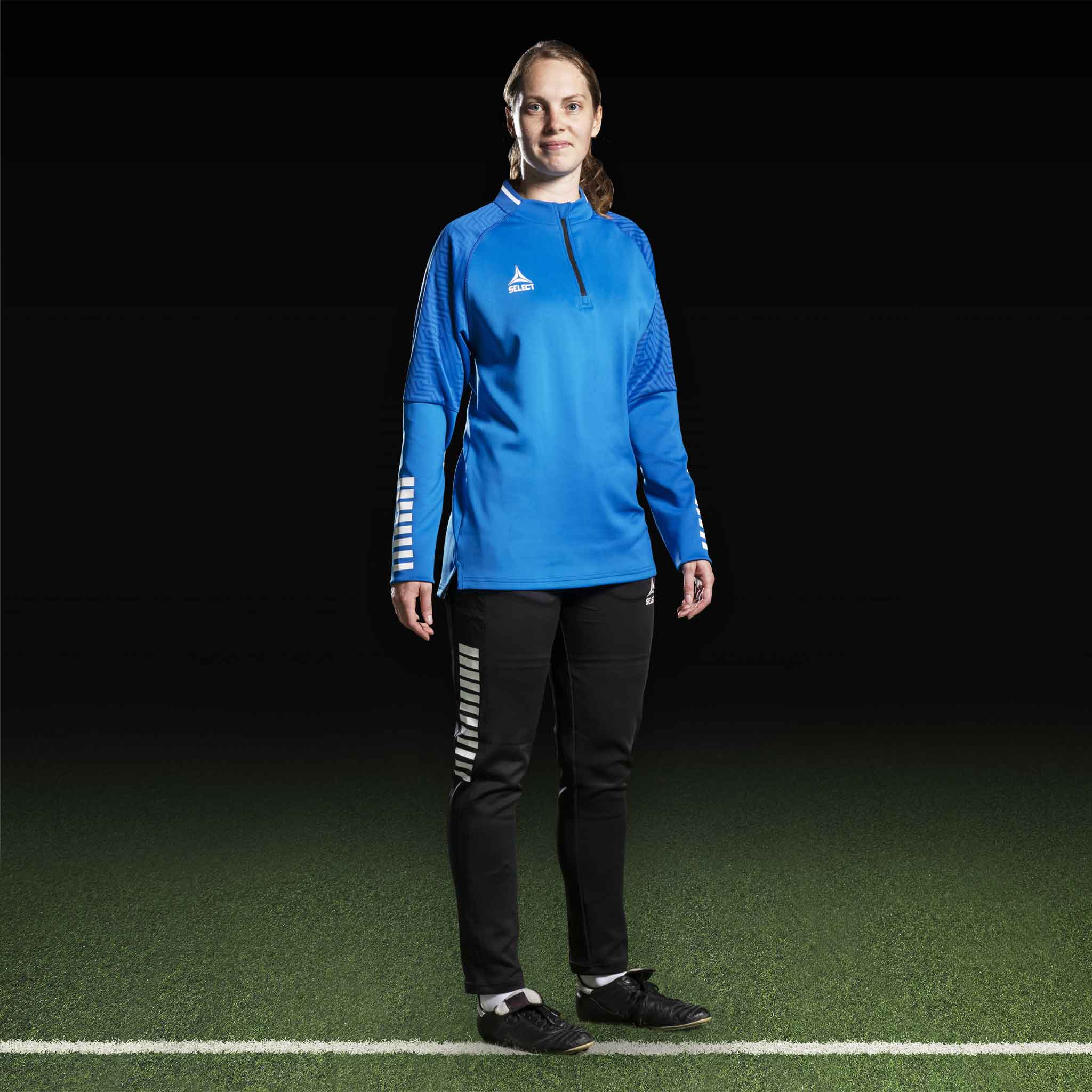 Kvinnlig fotbollsspelare i blå Training sweat 1/2 zip Monaco v24, Match & Training wear, med svarta byxor, framifrån.