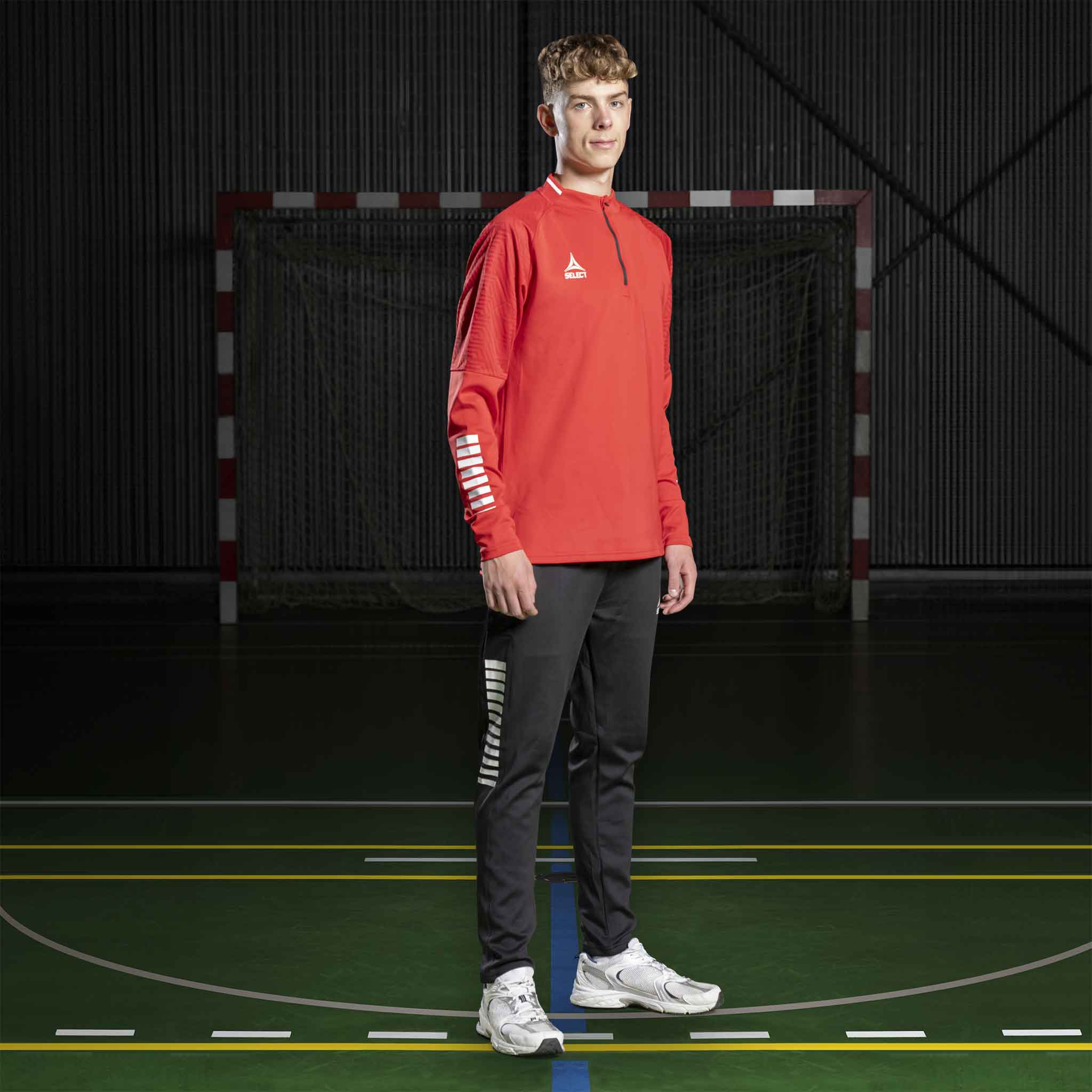 Manlig handbollsspelare i röd Training sweat 1/2 zip Monaco v24 och svarta byxor, Match & Training wear, på plan.