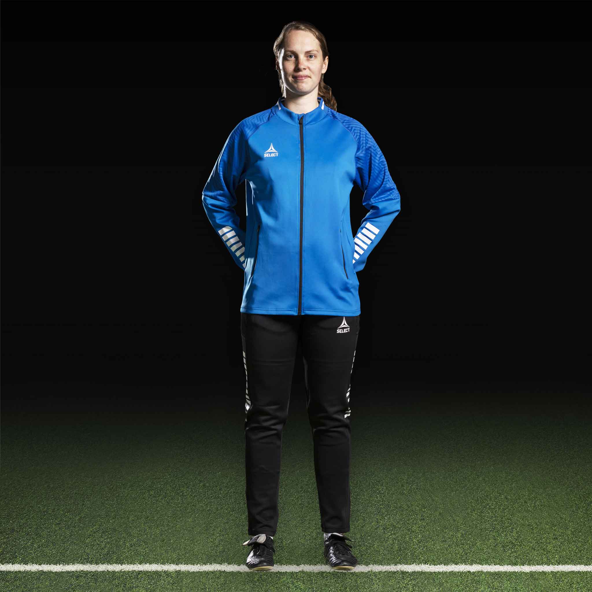 Kvinnlig fotbollsspelare i blå Zip jacket Monaco v24 och svarta byxor, Match & Training wear, framifrån.