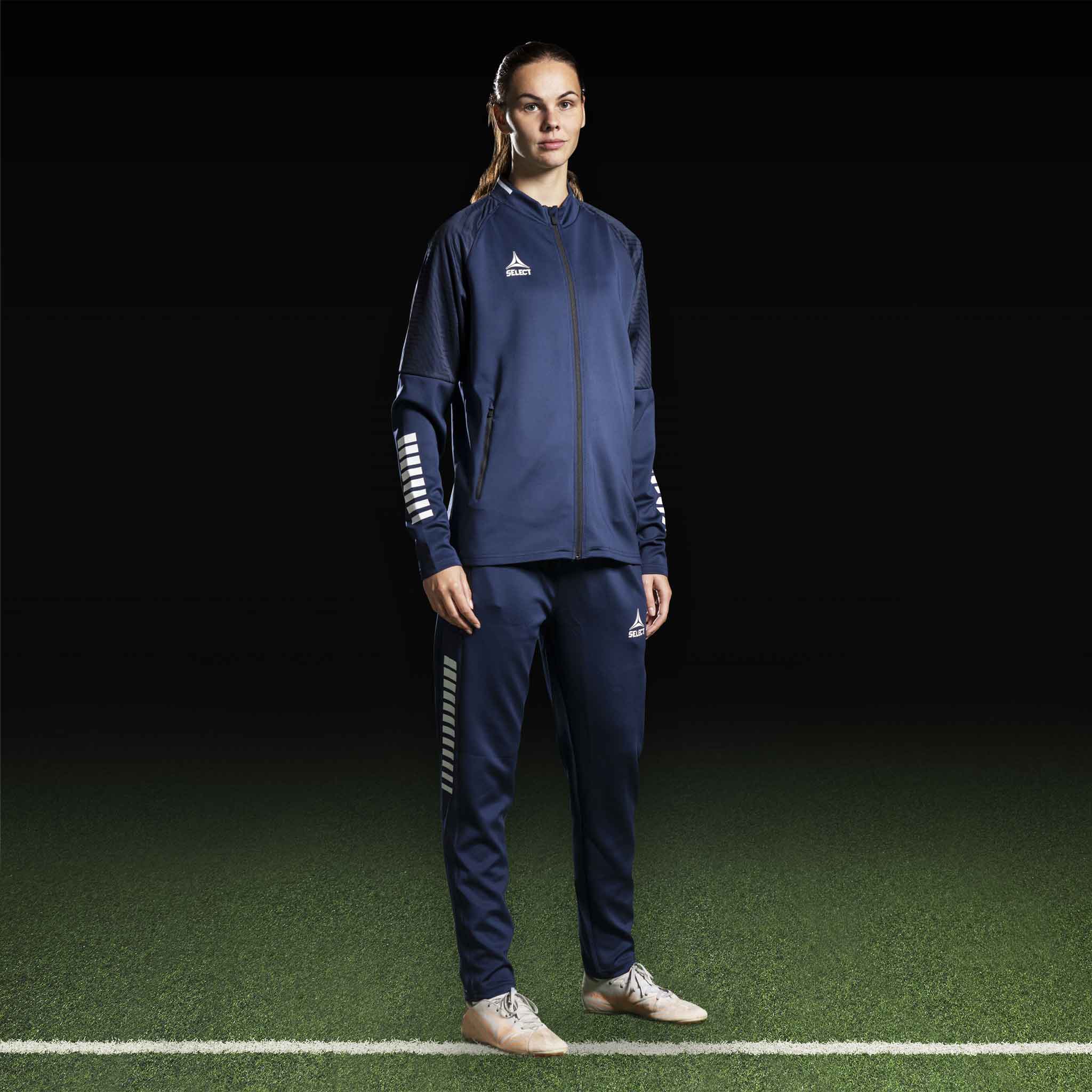 Kvinnlig fotbollsspelare i marinblå och vit Zip jacket Monaco v24, Match & Training wear, framifrån på plan.