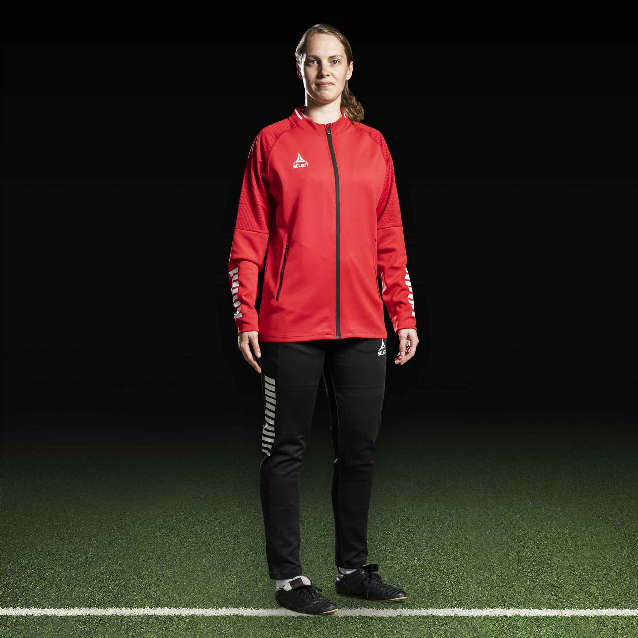 Kvinnlig fotbollsspelare i röd Zip jacket Monaco v24 och svarta byxor, Match & Training wear, framifrån.