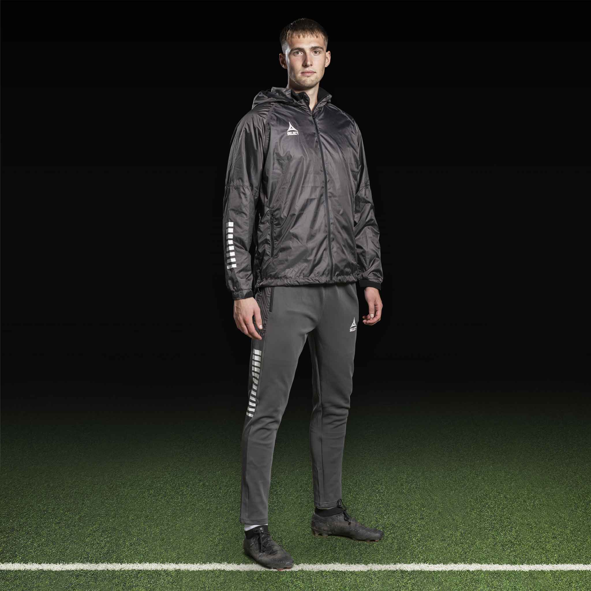 Manlig fotbollsspelare i grå Training pants Regular Fit Monaco v24 och svart jacka, Match & Training wear, framifrån.