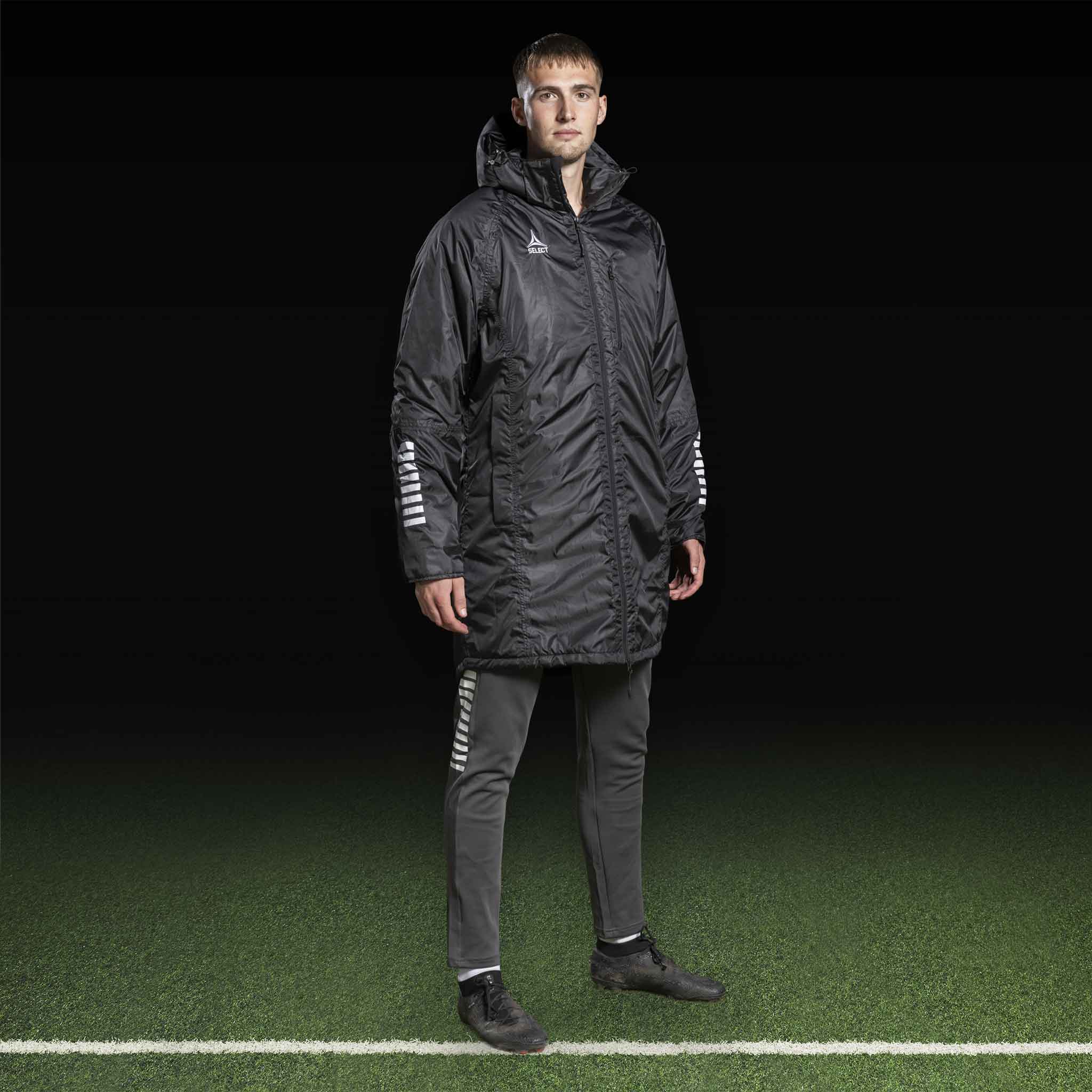 Manlig fotbollsspelare i svart Coach jacket Monaco v24 med grå byxor, Match & Training-kläder.
