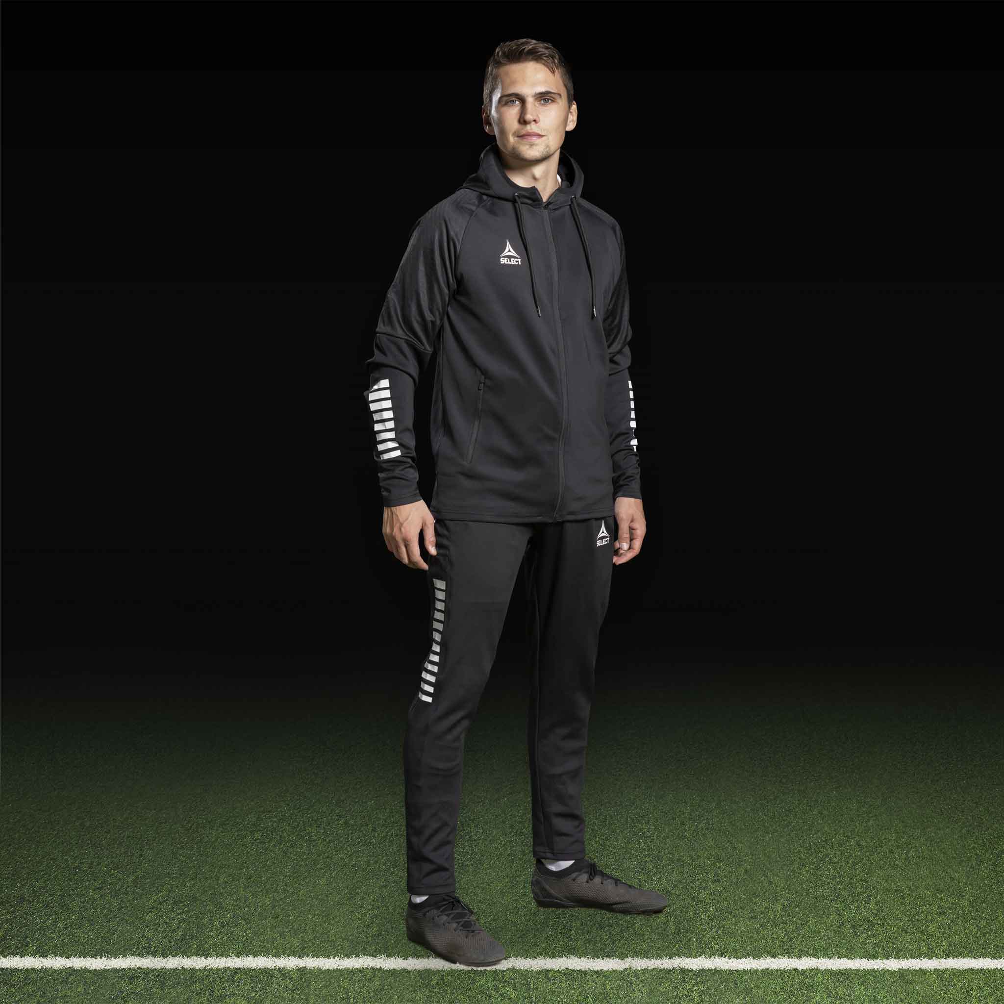 Manlig fotbollsspelare i svart Zip hoodie Monaco v24, Match & Training wear, med vita detaljer på ärmarna.