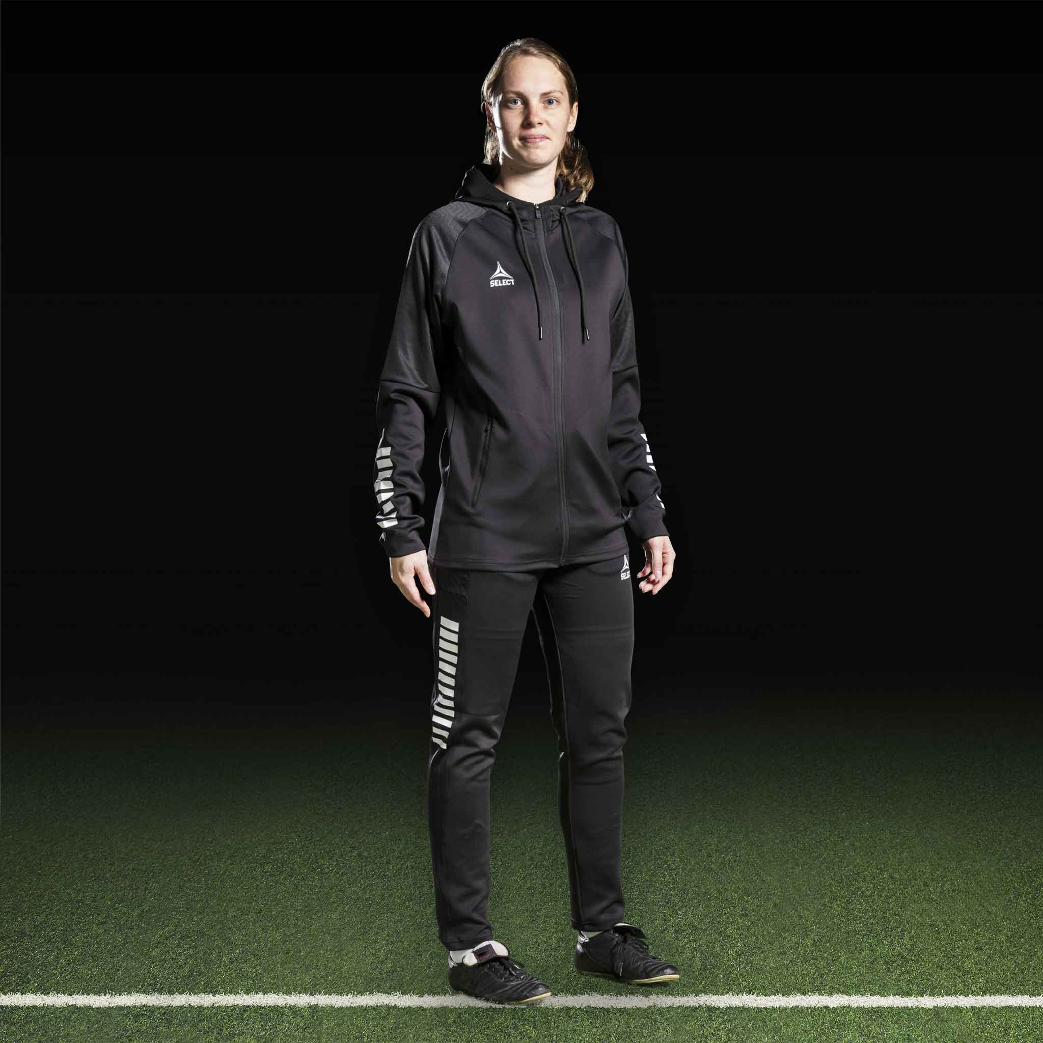 Kvinnlig fotbollsspelare i svart-vit Zip hoodie Monaco v24, Match & Training wear, framifrån på planen.