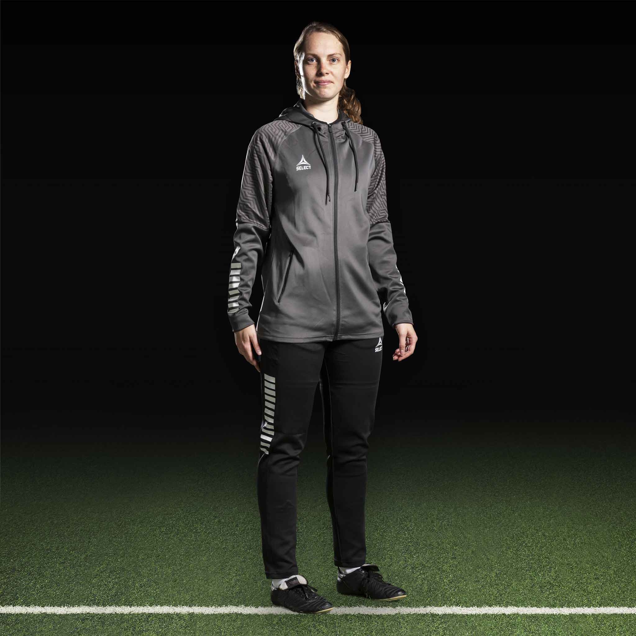 Kvinnlig fotbollsspelare i grå Zip hoodie Monaco v24 och svarta byxor, Match & Training-kläder.