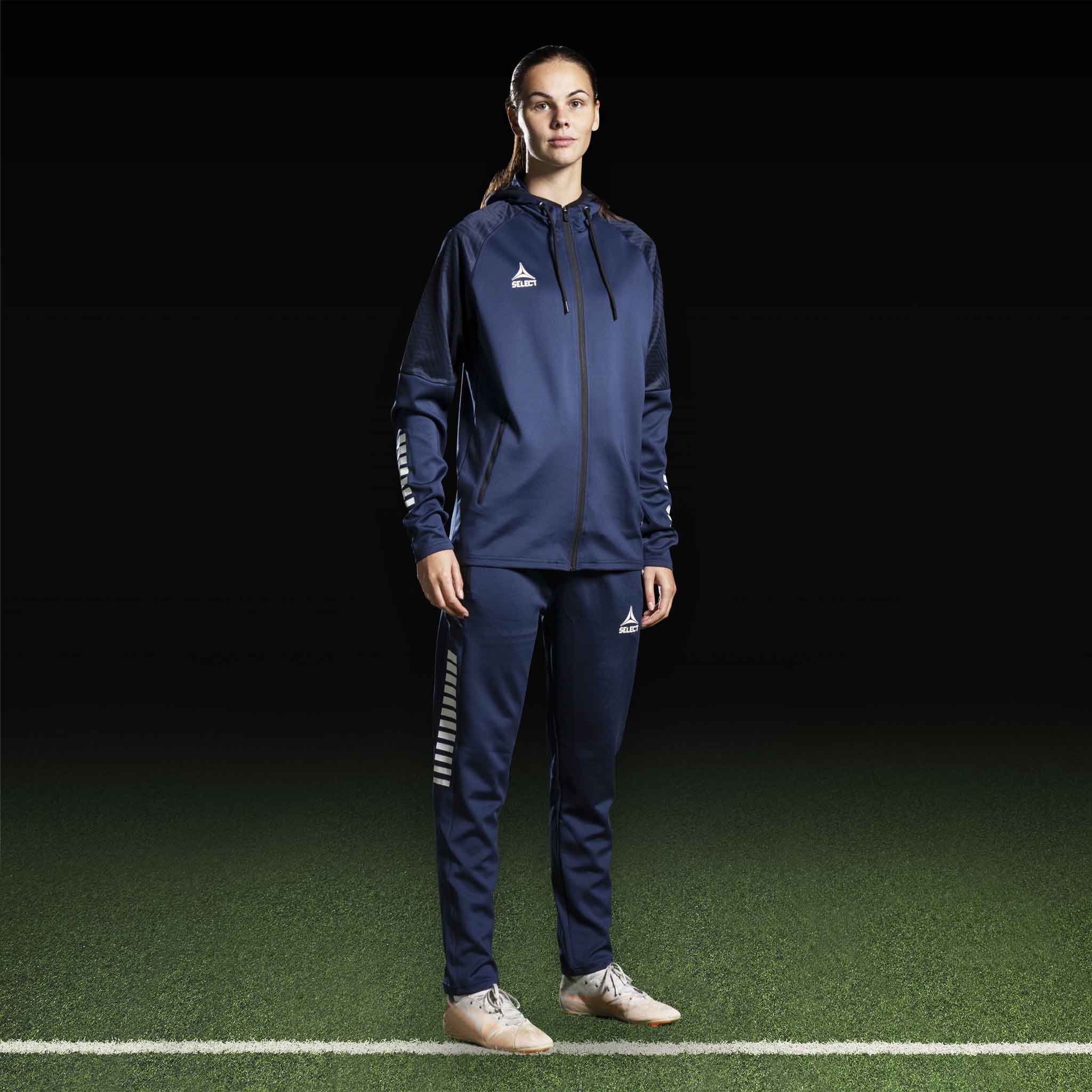 Kvinnlig fotbollsspelare i marinblå Zip hoodie Monaco v24, Match & Training wear, framifrån med vita logodetaljer.