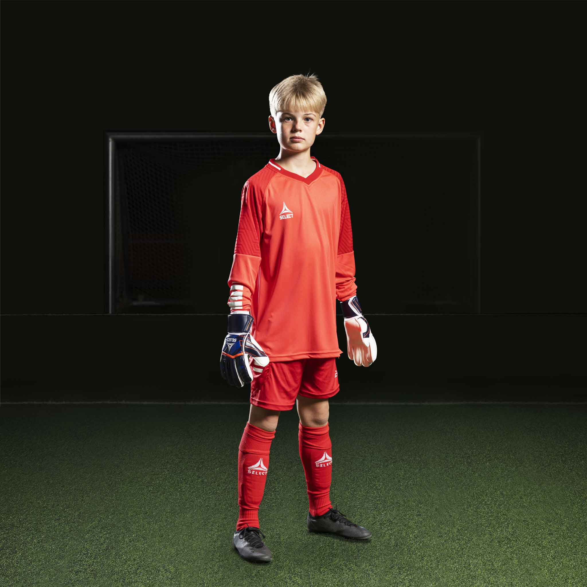 Pojke fotbollsspelare i röd Goalkeeper shirt Monaco v24, målvaktskläder, med matchande shorts och strumpor.