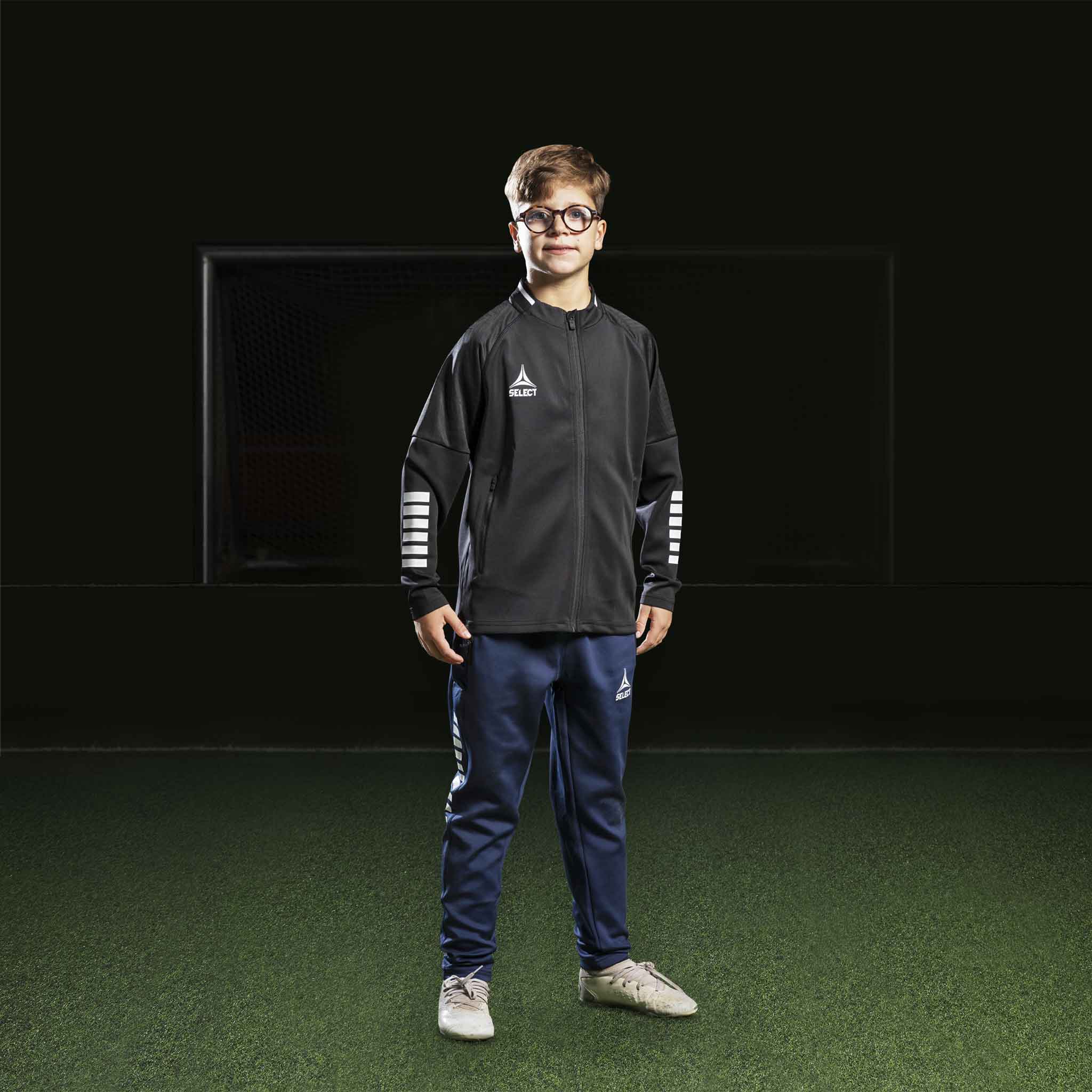 Pojke fotbollsspelare i svart Zip jacket Monaco v24 och marinblå byxor, Match & Training wear, framifrån.