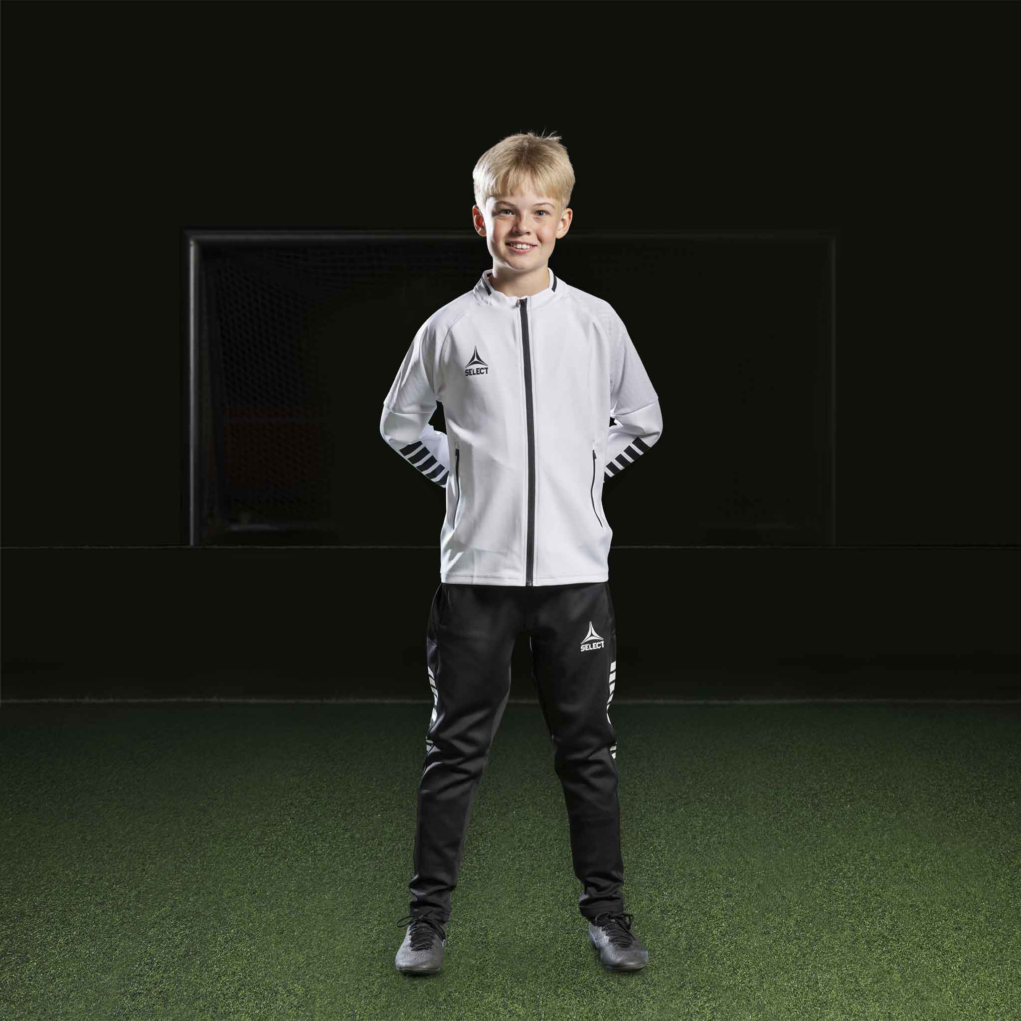 Pojke fotbollsspelare i vit Zip jacket Monaco v24 och svarta byxor, Match & Training wear, framifrån.