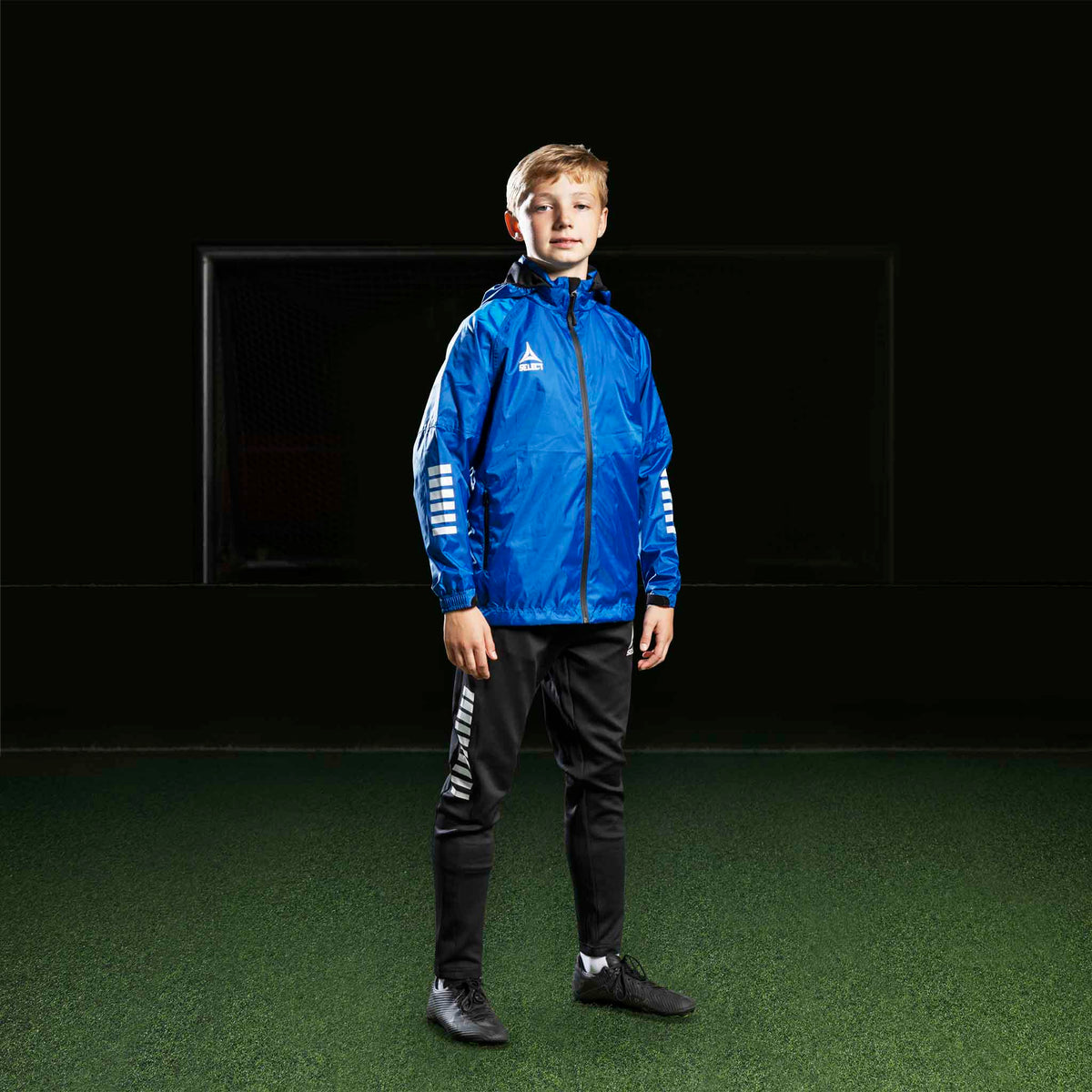 Fotbollsspelande pojke i blå jacka och svarta Training pants Regular Fit Monaco v24, Match & Training wear.