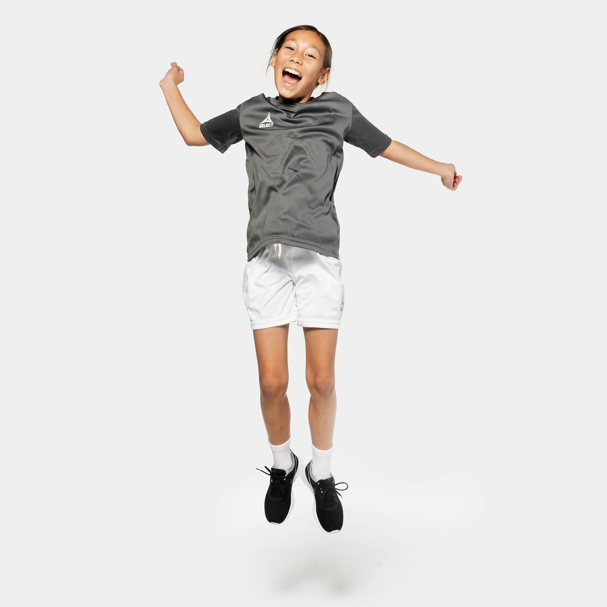 Pojke fotbollsspelare hoppar i grå tröja och vita Player shorts Pisa från Match & Training wear-kollektionen.