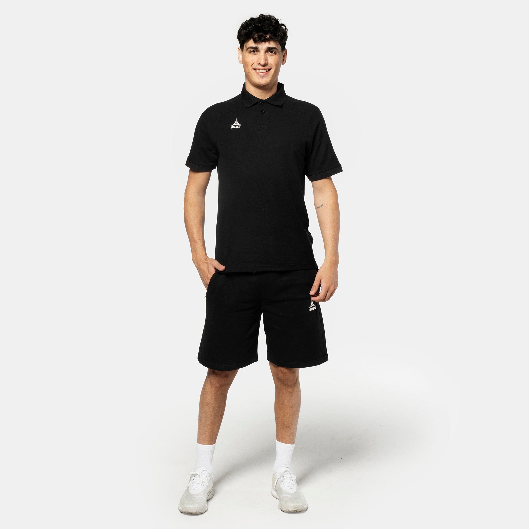 Manlig fotbollsspelare i svarta Sweat shorts Oxford v25 fritidskläder, framifrån med matchande pikétröja och vita sneakers.