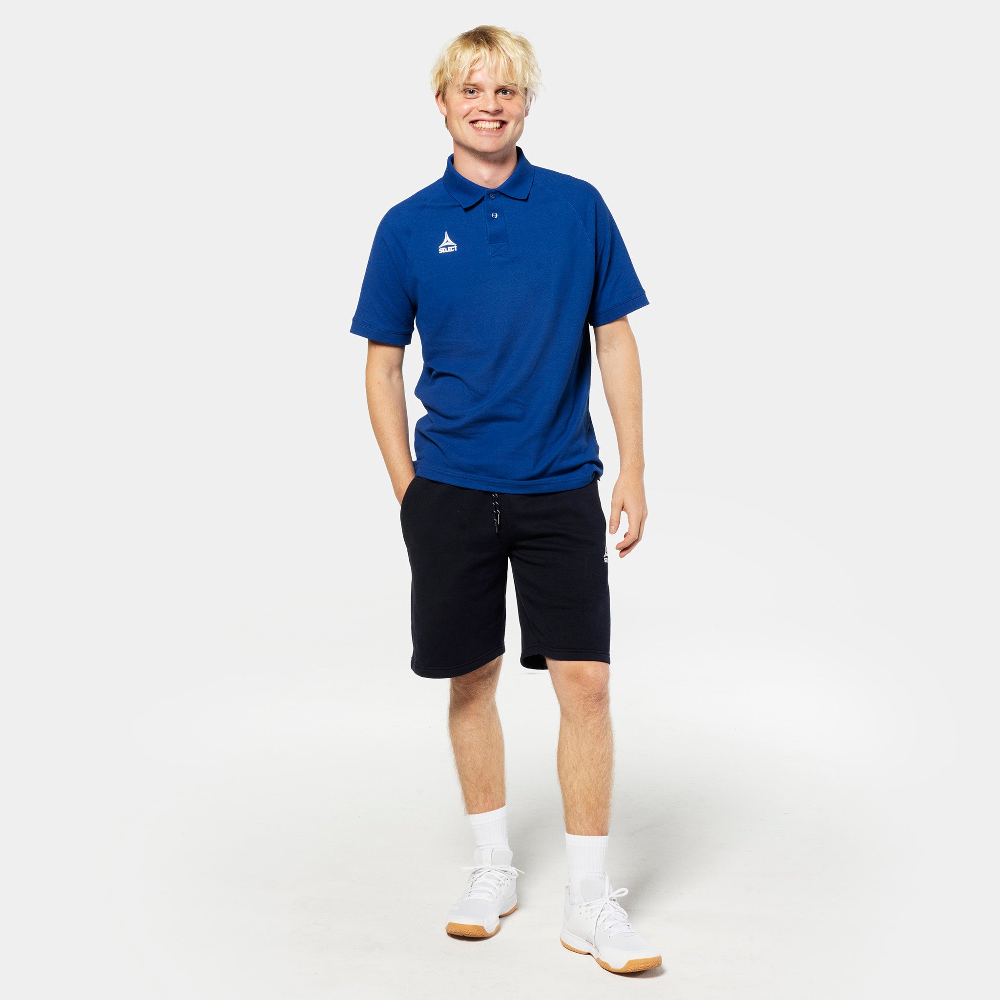 Manlig fotbollsspelare i blå piké och svarta Sweat shorts Oxford v25, fritidskläder, framifrån.