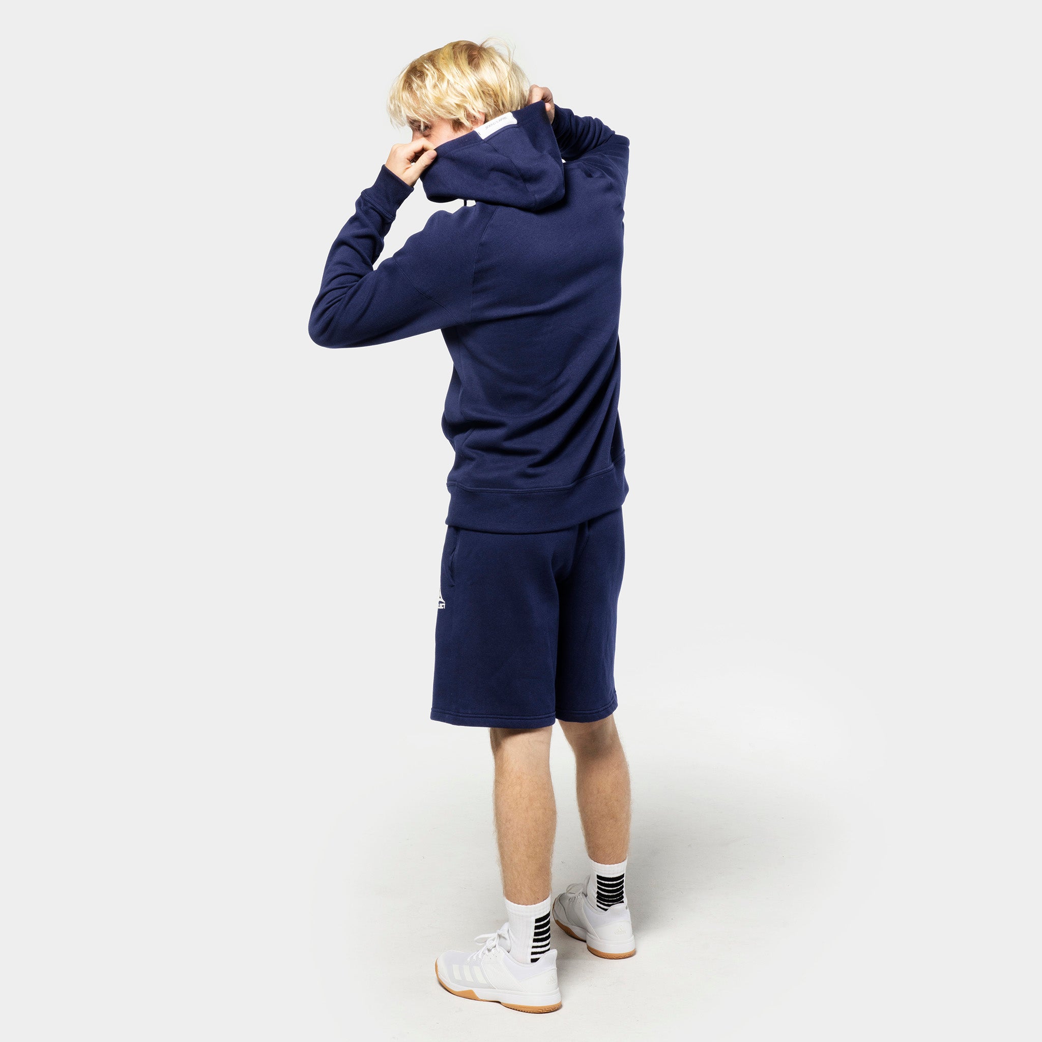 Bakifrån av manlig fotbollsspelare i marinblå Sweat shorts Oxford v25 och matchande hoodie, fritidskläder.
