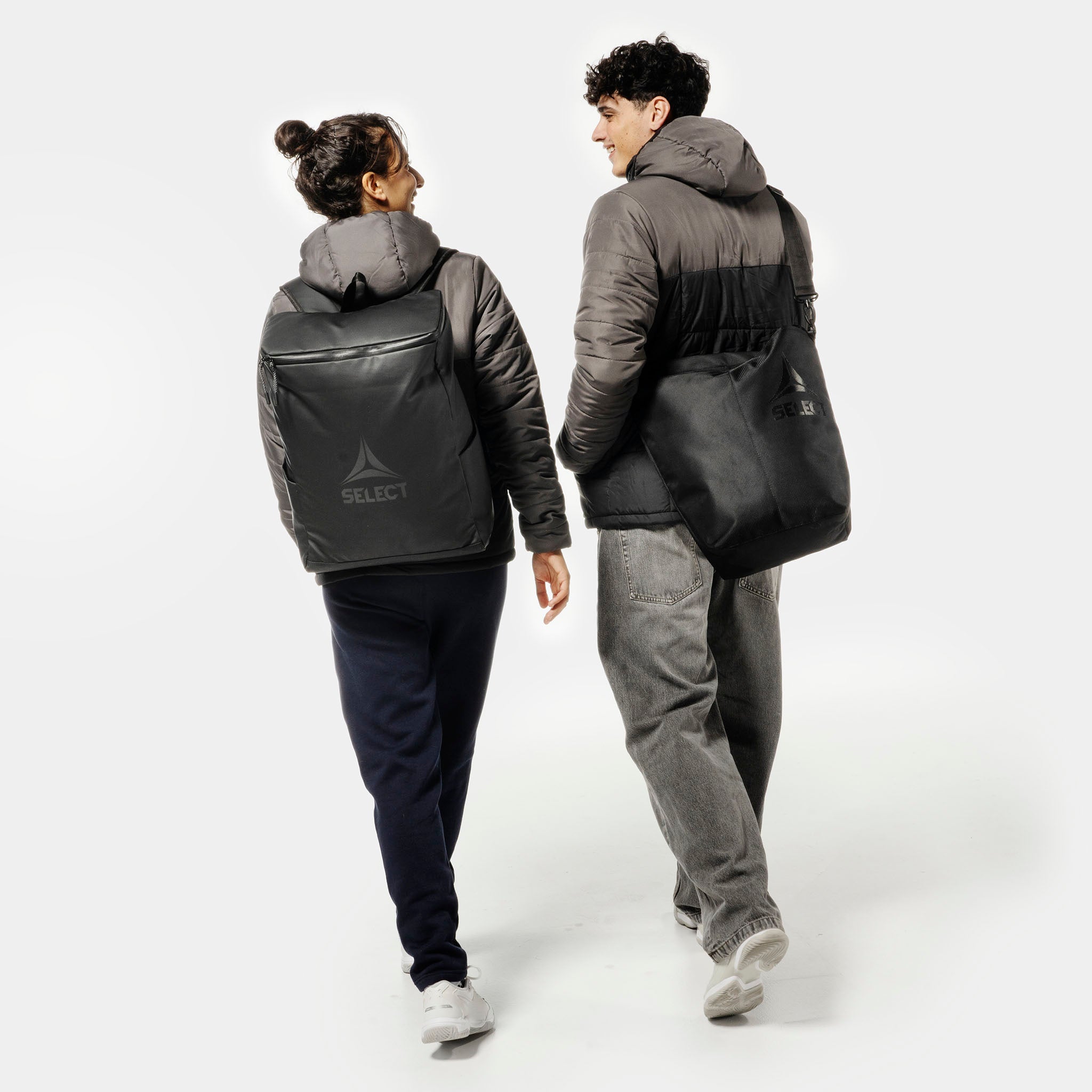 Kvinna och man fotbollsspelare med svarta Crossbody v25 sportväskor, bakifrån.