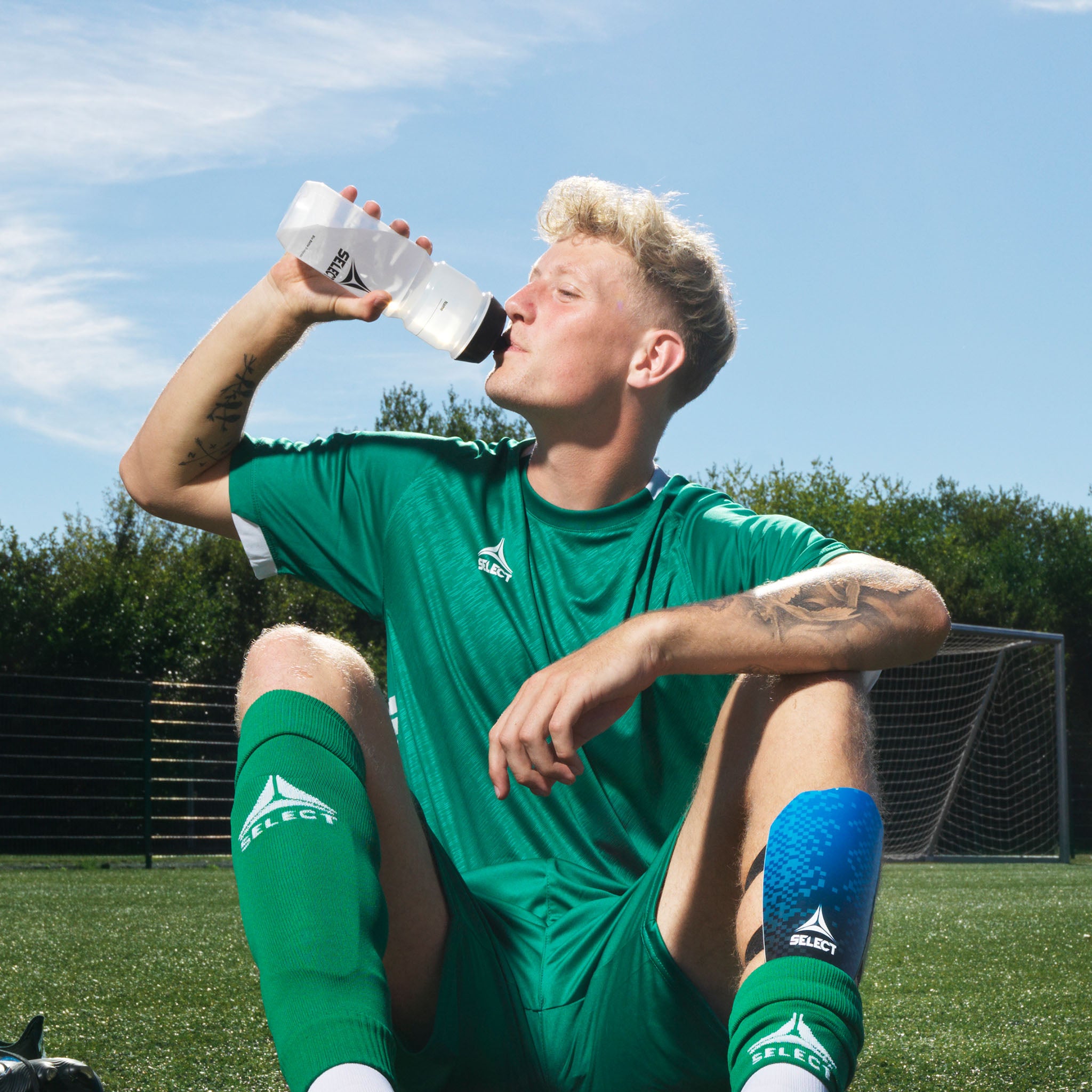 Vit Select v21 vattenflaska med röd detalj, använd av en fotbollsspelare på planen. Övrig lagutrustning & träningsutrustning.