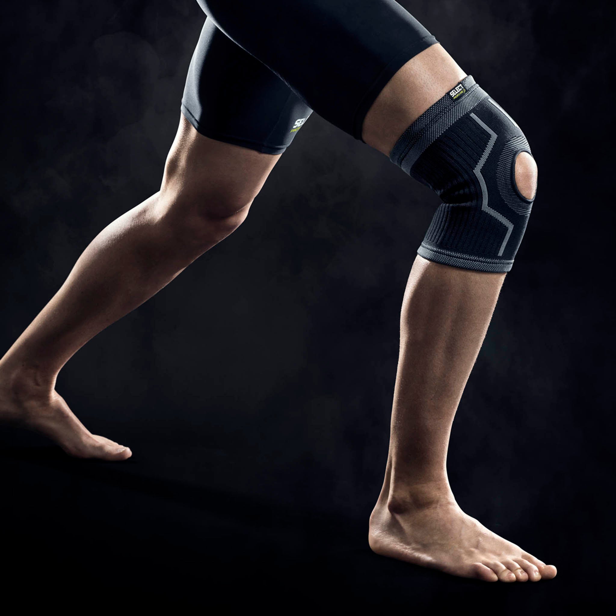 Mand iført sort Knee support w/hole, en sportsstøtte, på knæet. Modelfoto der viser forsiden af støtten.